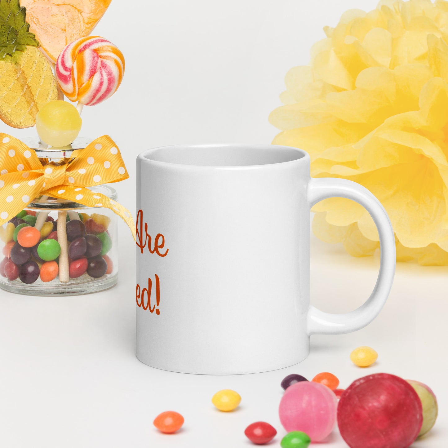 White mug with You Are Blessed text, surrounded by colorful candies and flowers on a white background.